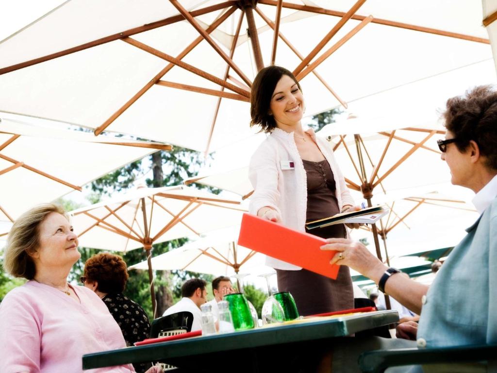 a woman talking to a group of people under an umbrella at Mercure Szekesfehervar Magyar Kiraly in Székesfehérvár
