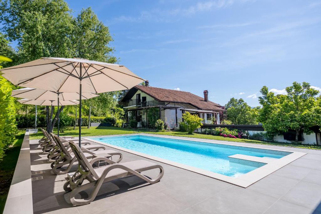 a pool with chairs and an umbrella and a house at Villa Bella, villa with heated Pool in Cerovlje