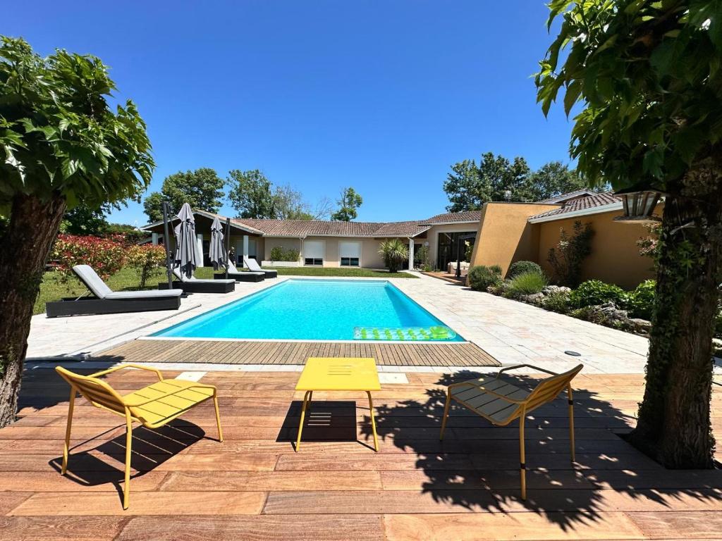 une piscine avec deux chaises et une table et des chaises jaunes dans l'établissement Villa avec piscine et spa sur la route des vins, à La Brède