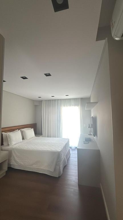 a white bedroom with a bed and a window at Flat TOP - No Praia Brava Hotel na ilha a beira mar in Florianópolis