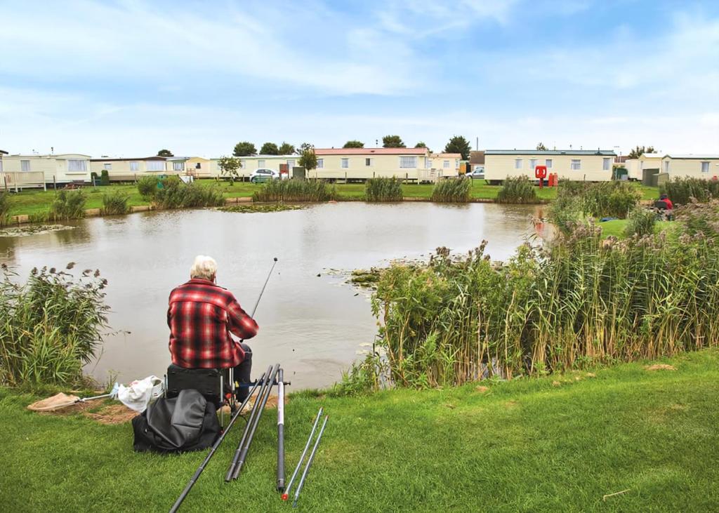a man sitting on the grass fishing in a pond at Towervans Caravan Park in Mablethorpe