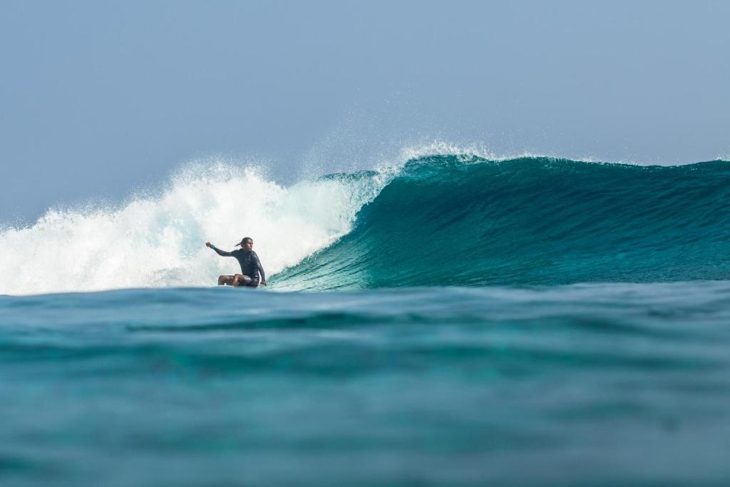 een man die op een surfplank in de oceaan op een golf rijdt bij TWIN PALMS 'Beach House' - New surf front location in Thulusdhoo