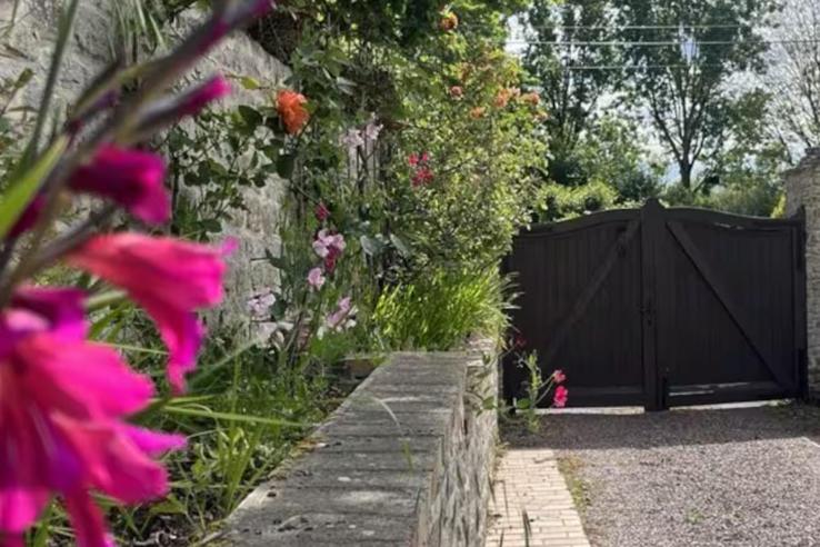 a black gate in a garden with pink flowers at Fabuleux studio à 2 pas du Canal de l'Orne in Hérouville-Saint-Clair