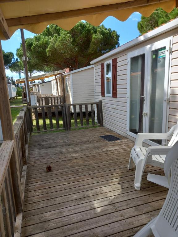 a deck with two white chairs and a house at mobilhome 232 tohapi marvilla in Torreilles