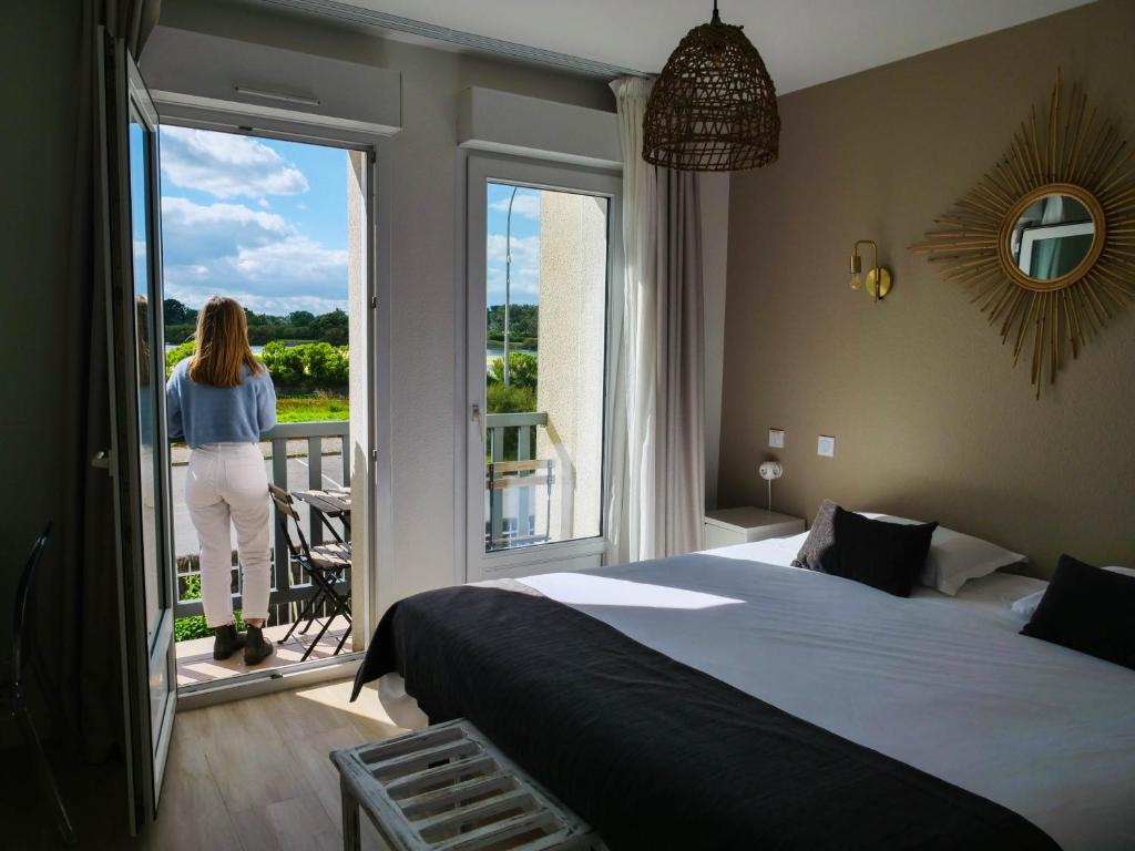 Eine Frau steht auf einem Balkon mit Blick aus einem Schlafzimmer in der Unterkunft Hotel La Licorne in Carnac