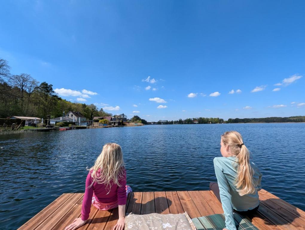 two girls sitting on a dock on a lake at Ferienhaus am See Wutzsee mit direktem Seezugang in Lindow