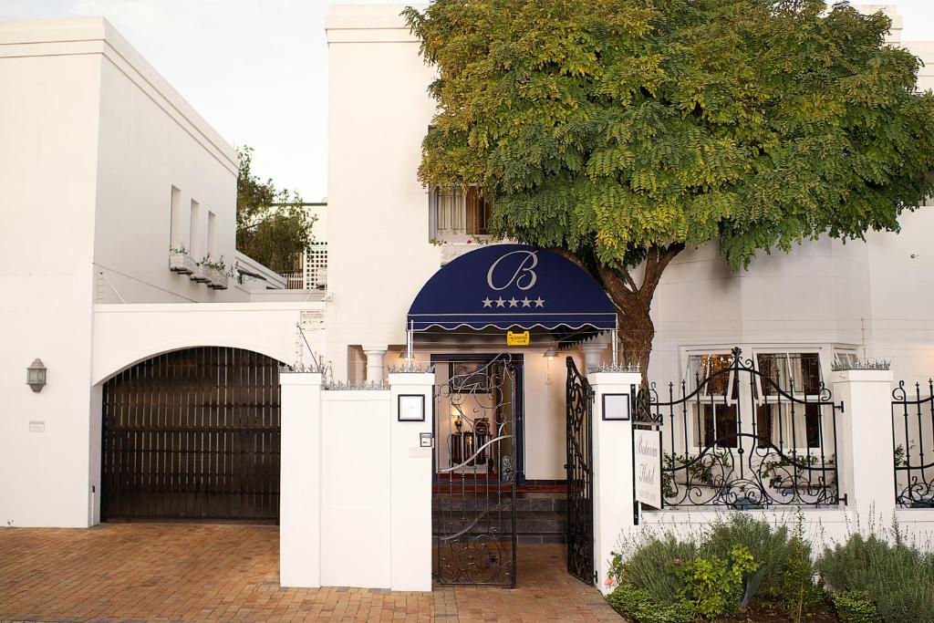 a white building with a black gate and a tree at Batavia Boutique Hotel in Stellenbosch