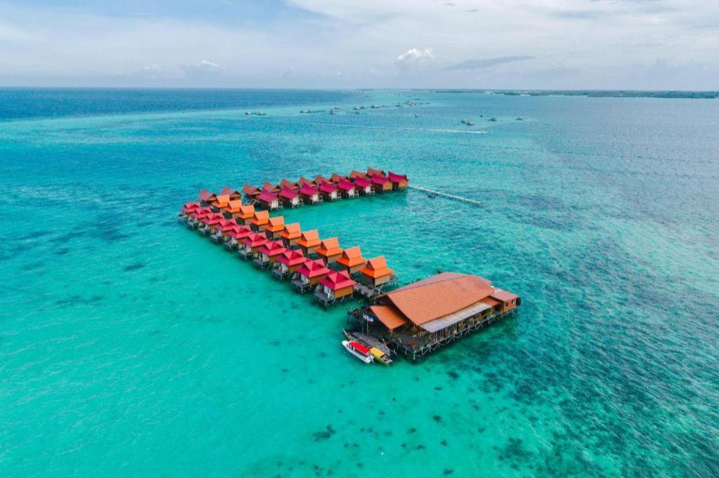 an island in the ocean with red and orange umbrellas at SAND BAY RESORT SEMPORNA in Pulau Sabangkat