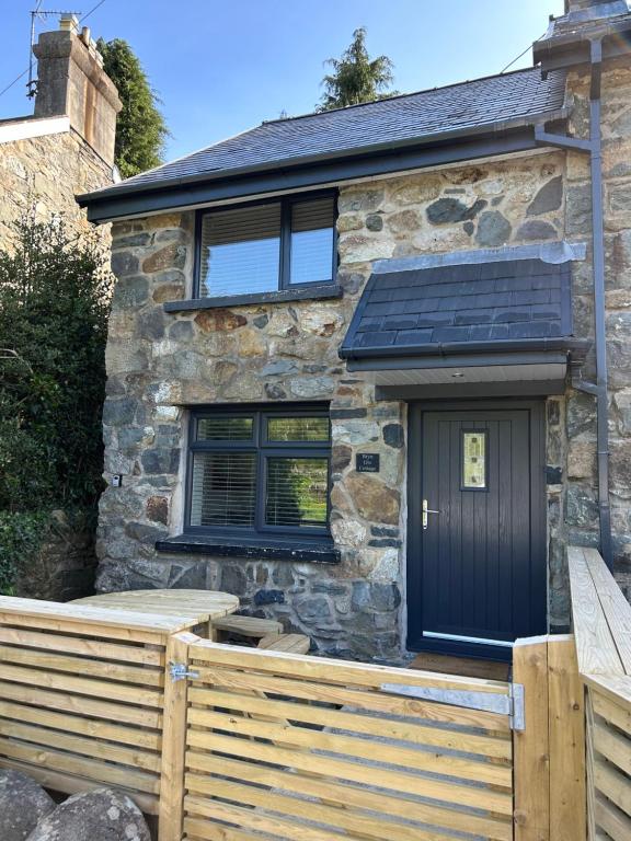 une maison en pierre avec une porte noire et une clôture en bois dans l'établissement Bryn Glo Cottage, à Capel-Curig