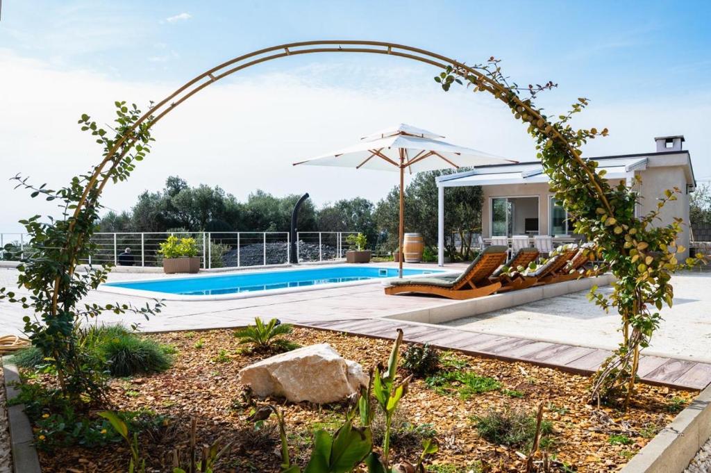 an arch over a swimming pool with chairs and an umbrella at Skriveni dragulj - A Peaceful Oasis with a Sea View in Trogir