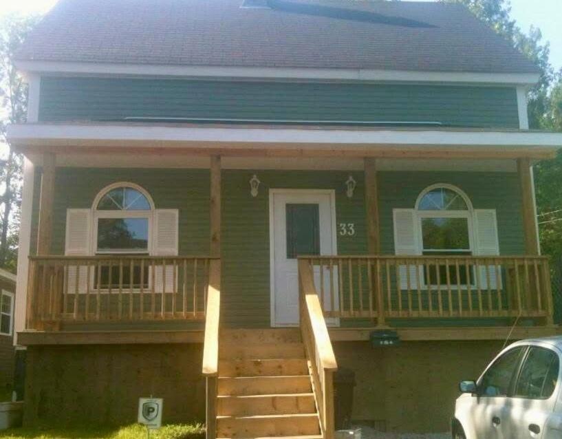 a green house with a porch and a deck at Townsite Comfort in Corner Brook
