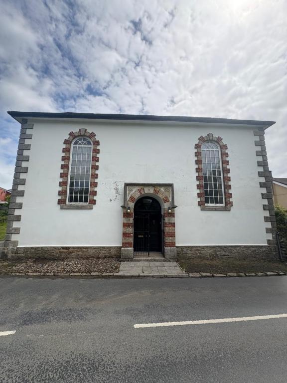 a white building with a door and two windows at Chapel House in Saint Cleer