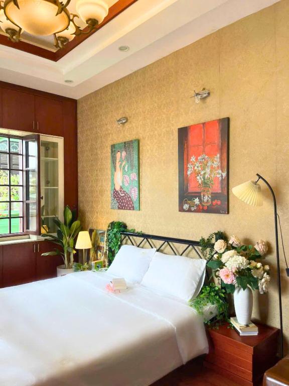 a bedroom with a large white bed and paintings on the wall at Ả home - Hồ tây, phòng lớn, ban công in Hanoi
