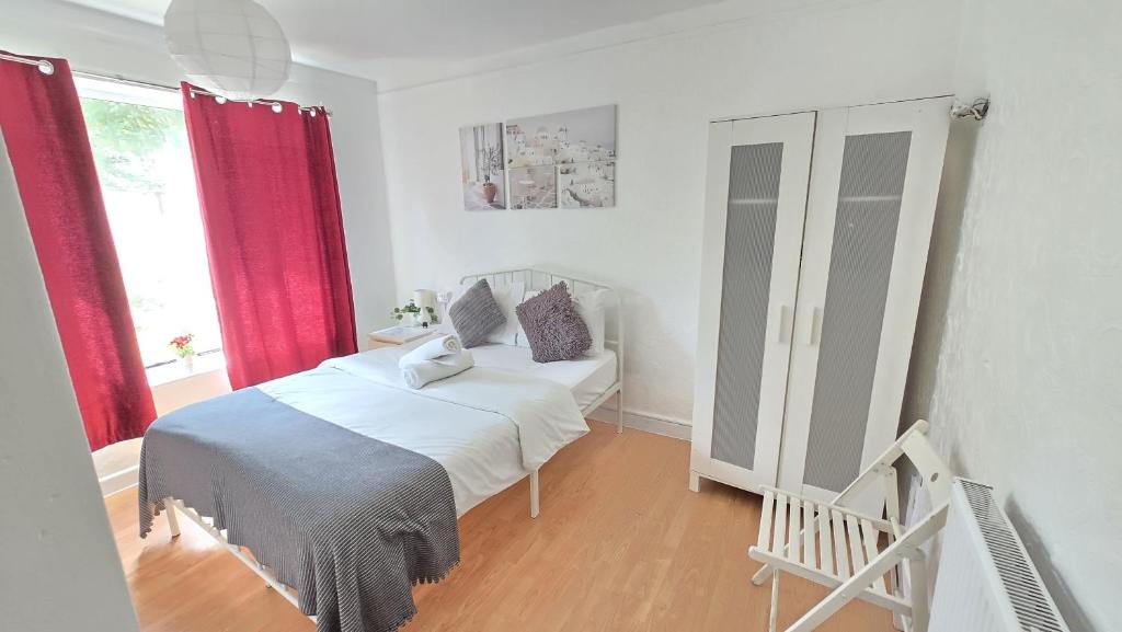 a bedroom with a white bed and red curtains at Canary wharf cottage in London
