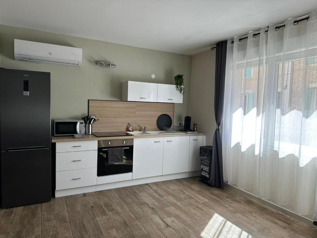 a kitchen with white cabinets and a black refrigerator at La Loge du Théâtre in Orange