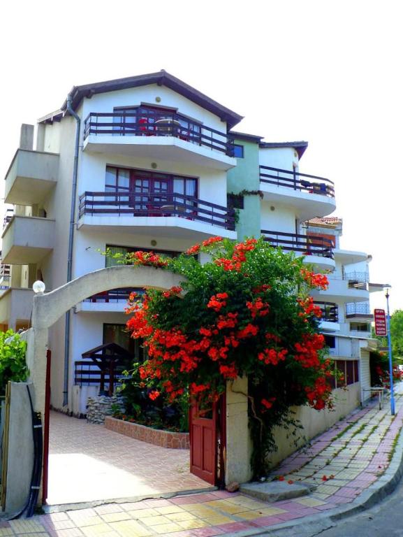 a white building with red flowers in front of it at Guest House Urdoviza in Kiten