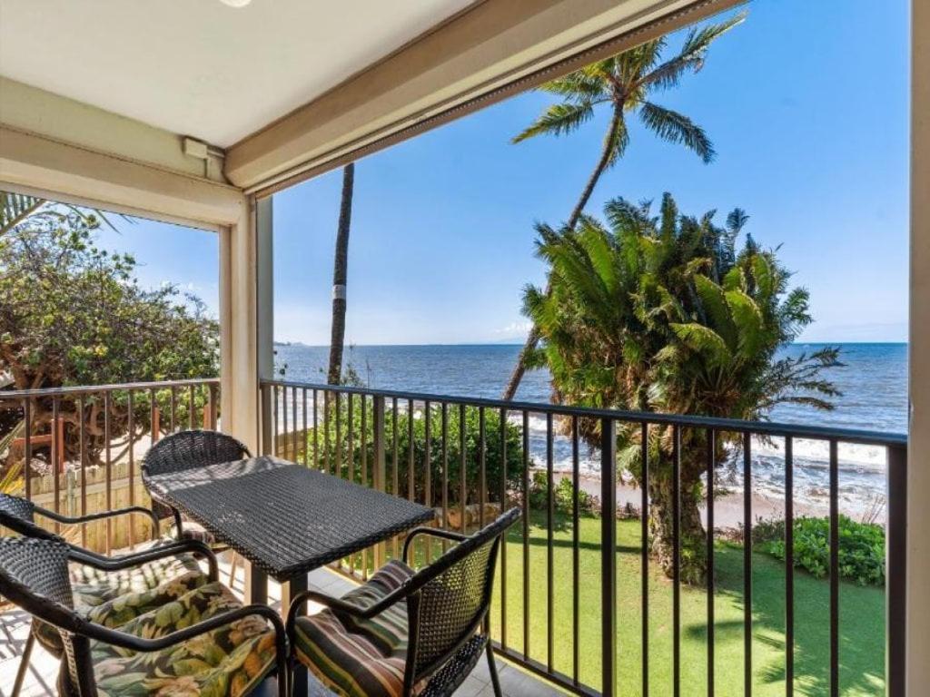 a balcony with a table and chairs and the ocean at KIHEI BEACH, #210 condo in Kihei