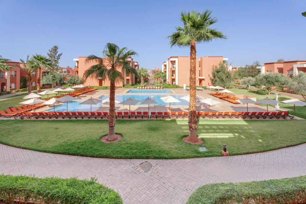 un complejo con piscina, palmeras y sombrillas en Zephyr Targa Marrakech, en Marrakech