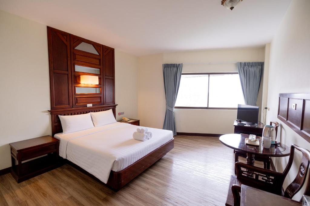 A bright double room with a curtained window, polished wood furniture, and a small sitting-and-drinks area.