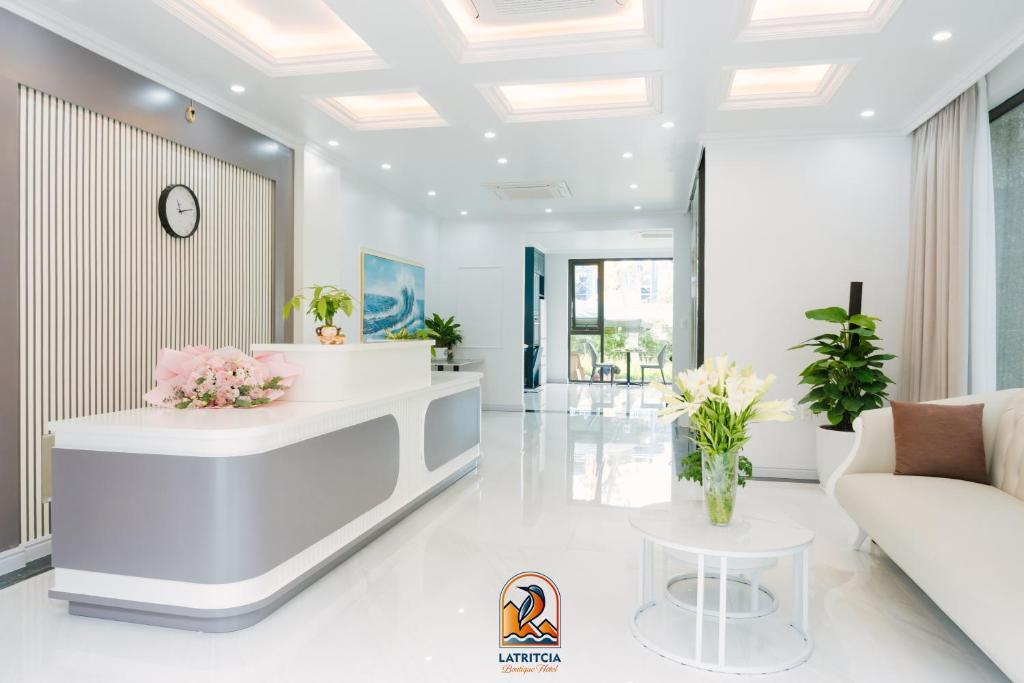 a white lobby with a reception desk and flowers at Latritcia Boutique Hotel in Cat Ba