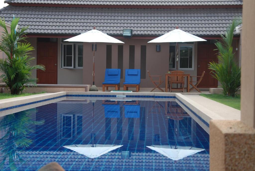 a swimming pool with blue chairs and umbrellas next to a house at Lanna Thai Villa Bed and Breakfast in Thoeng