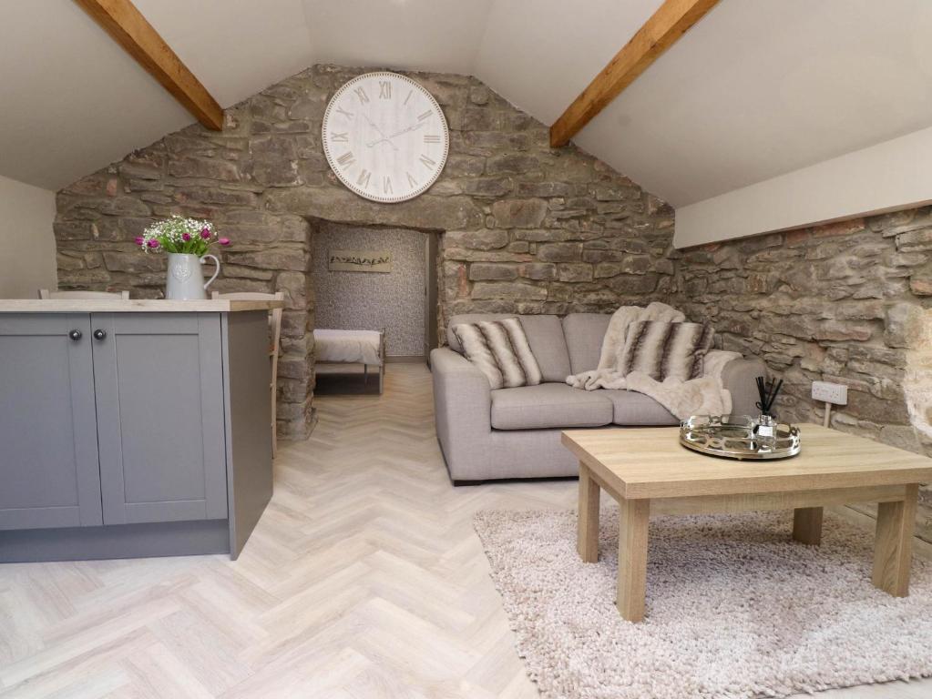 a living room with a couch and a clock on a stone wall at The Hayloft in Colwyn Bay