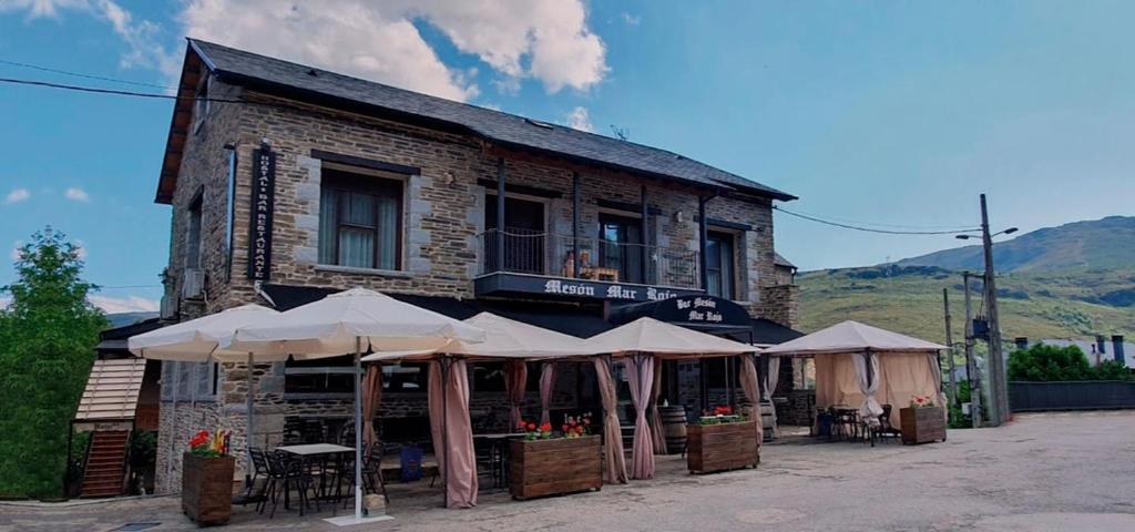 Un edificio con mesas y sombrillas delante. en Hostal Restaurante MarRojo Sanabria, en Requejo