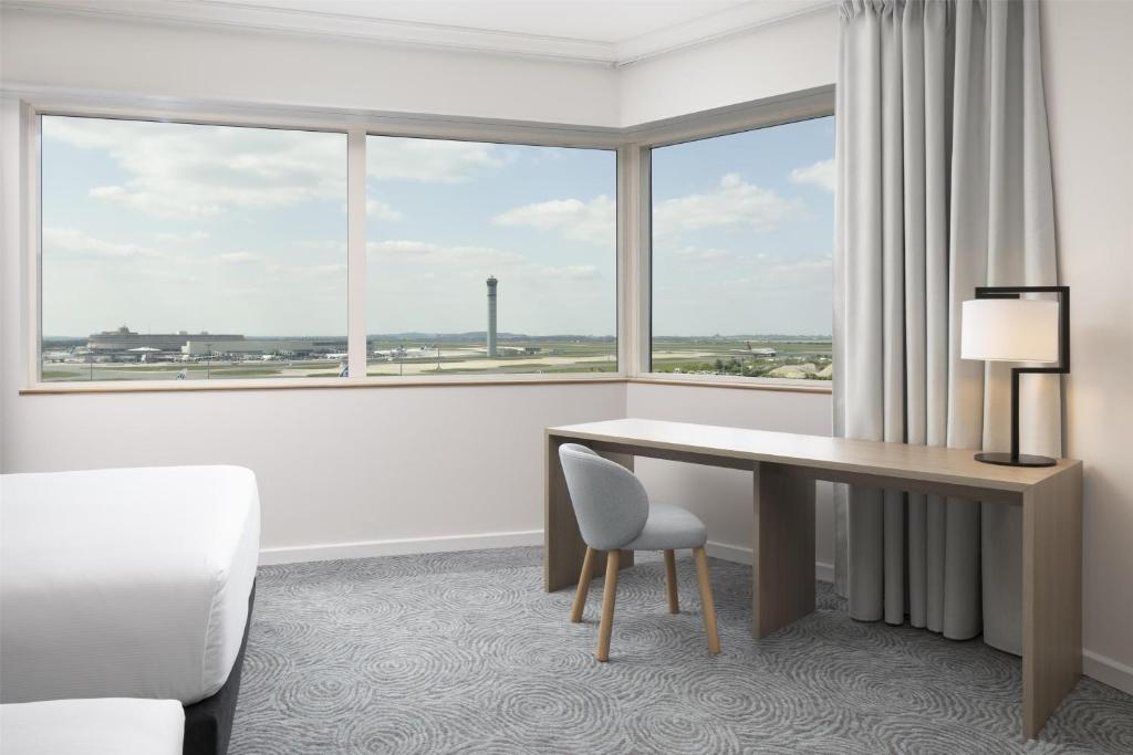 a hotel room with a desk and a large window at Hilton Paris Charles De Gaulle Airport in Roissy-en-France