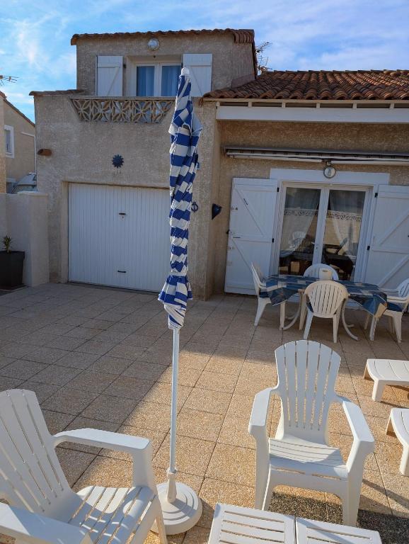 d'une terrasse avec des chaises blanches et un parasol bleu et blanc. dans l'établissement Maison de vacances climatisée 600m de la mer Cour privative et parking, à Port-la-Nouvelle