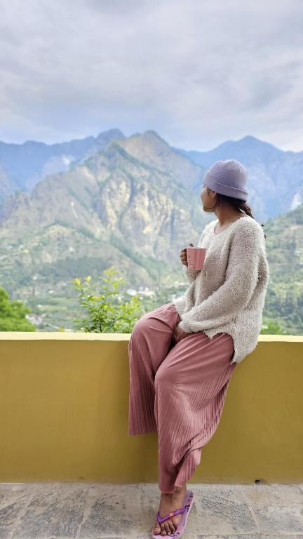 a woman sitting on a wall looking at a mountain at Kintsugi by Oztel in Kasol