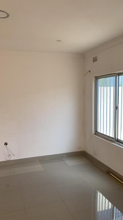 an empty room with a window and a tiled floor at Zimindo plaza in Mpemba