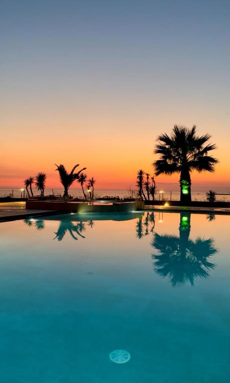a pool with palm trees in front of a sunset at Pachia Ammos Falasarna in Falasarna