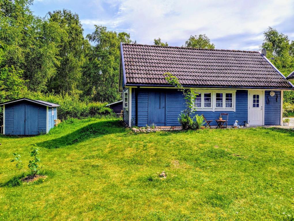 a blue house with a grassy yard in front of it at Cosy Cabin close to Lake in Ludvigsborg