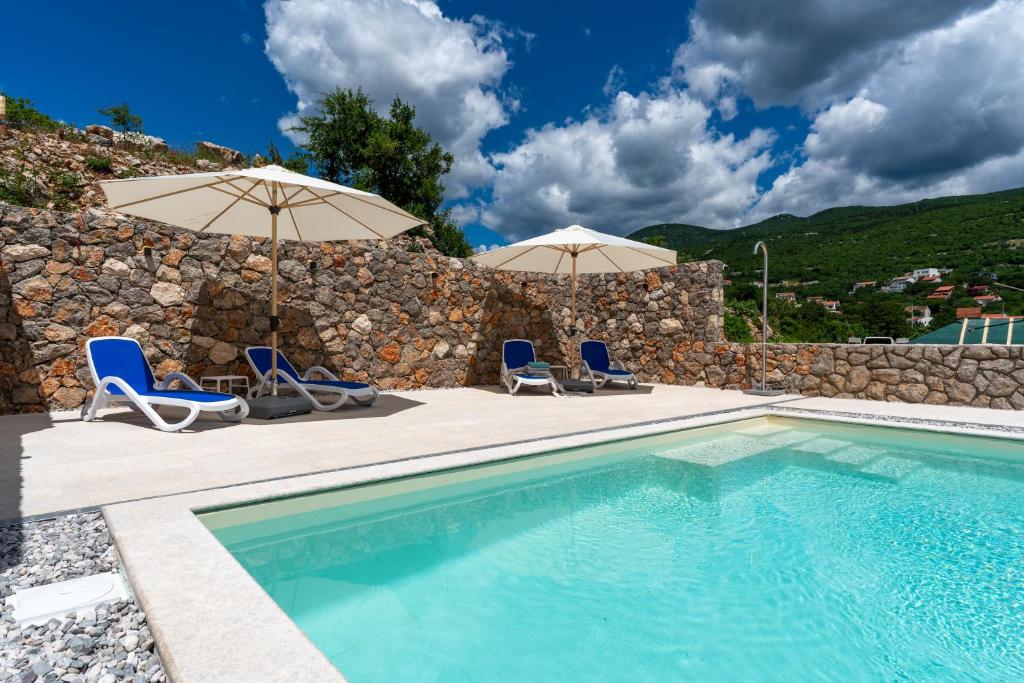 a swimming pool with two chairs and umbrellas at Ferienhaus Sana in Klenovica