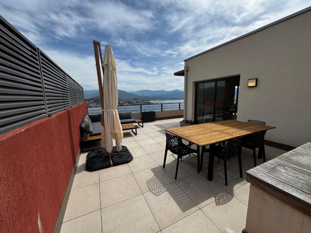 un balcon avec une table et des chaises en bois et un parasol dans l'établissement Superbe T3 avec rooftop Vue mer et montagne Ajaccio, à Ajaccio