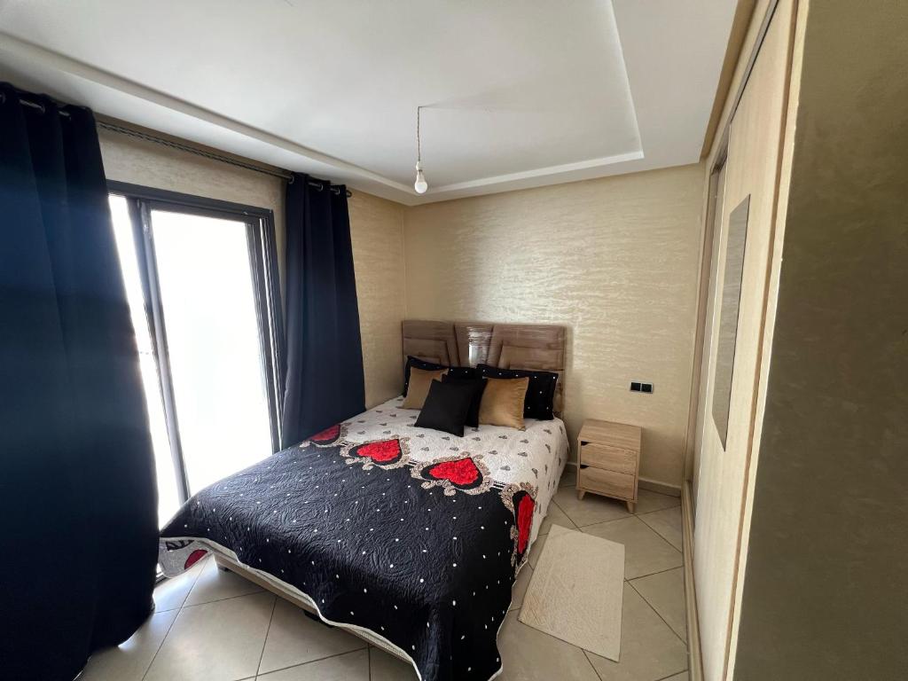 ein Schlafzimmer mit einem Bett mit einer schwarzen Bettdecke und einem Fenster in der Unterkunft Résidence les belles Rives in Bouznika