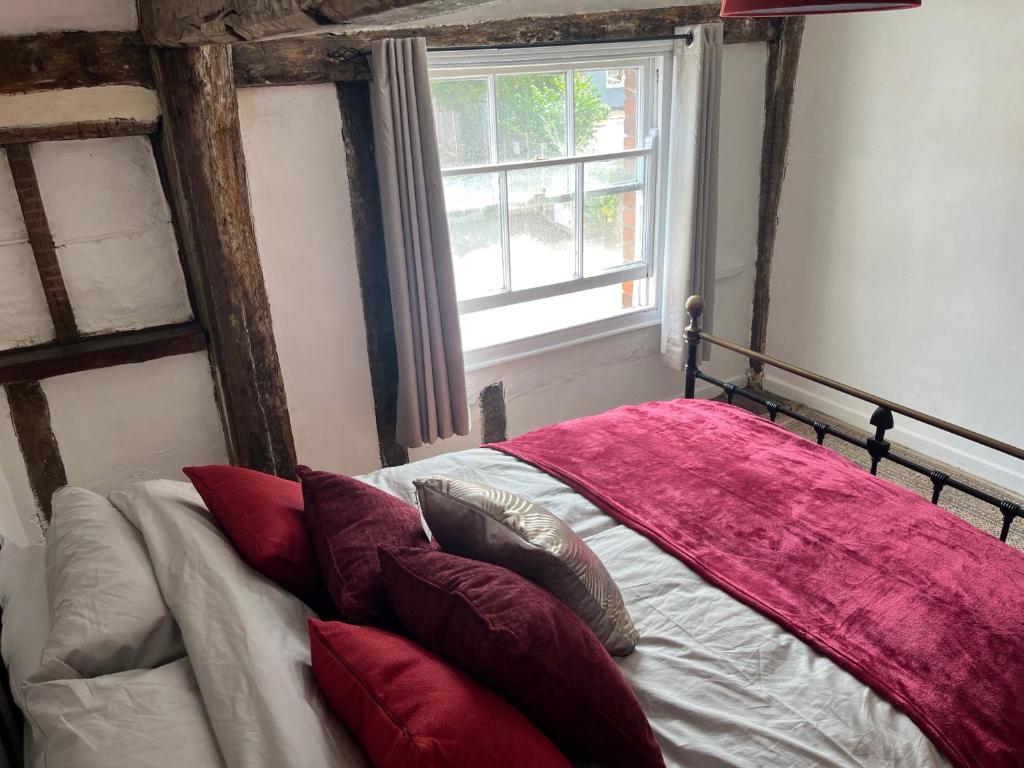 a bedroom with a bed with red pillows and a window at Harleston Norfolk Suffolk border Historic Cottage in Harleston