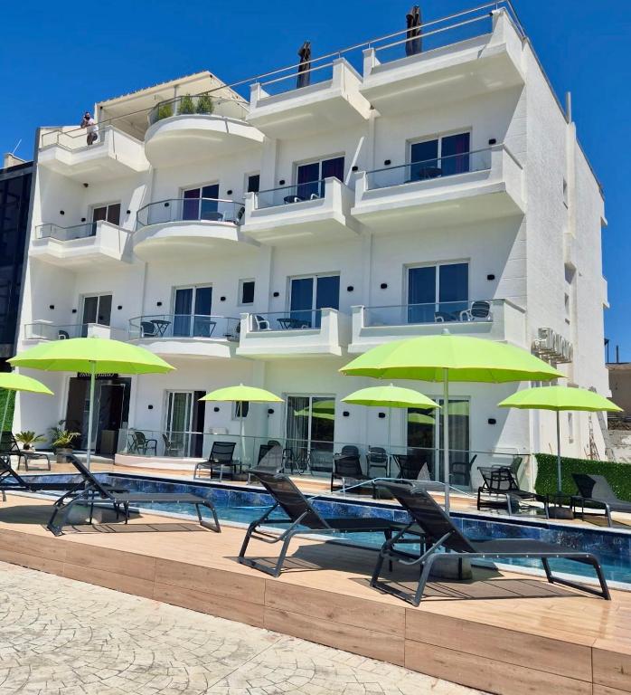 a large white building with green umbrellas and a pool at Galaxy Hotel in Ksamil