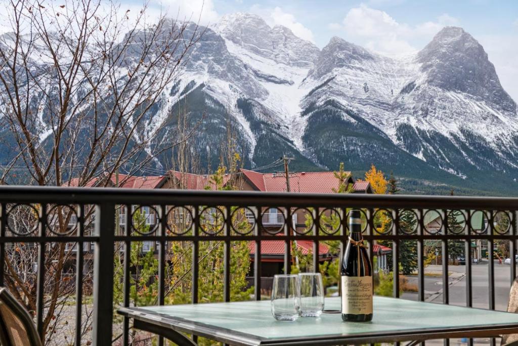 a bottle of wine on a table on a balcony with mountains at Chic Mountain View - Pool & HotTub - Fireplace - BBQ! in Canmore