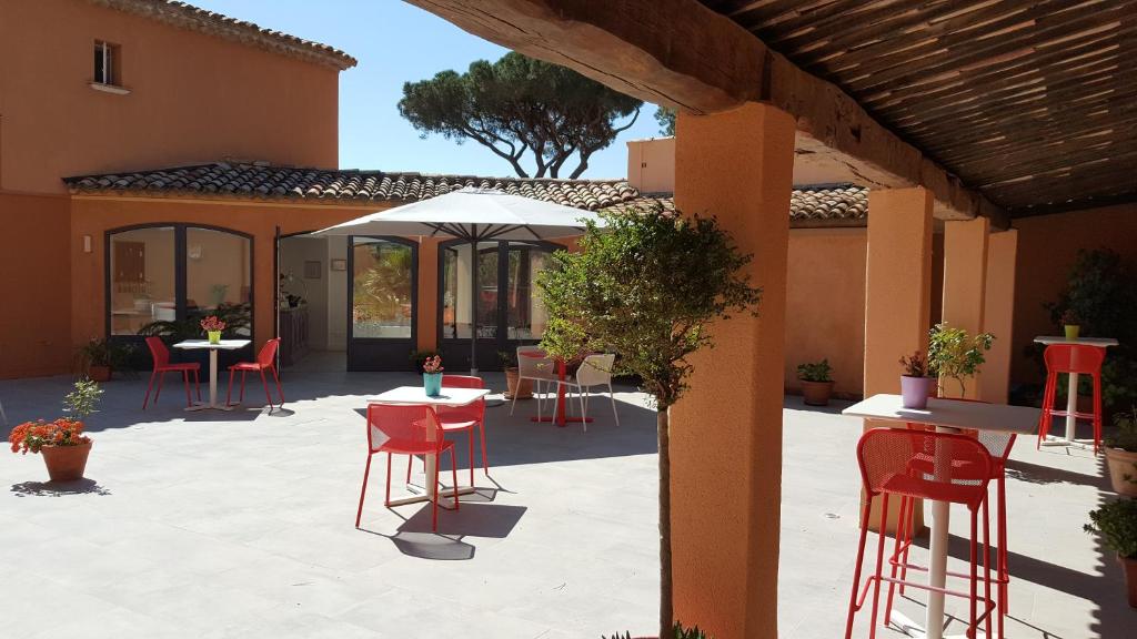 a patio with red chairs and tables and an umbrella at Hôtel les Bouis - Vue mer in Saint-Tropez