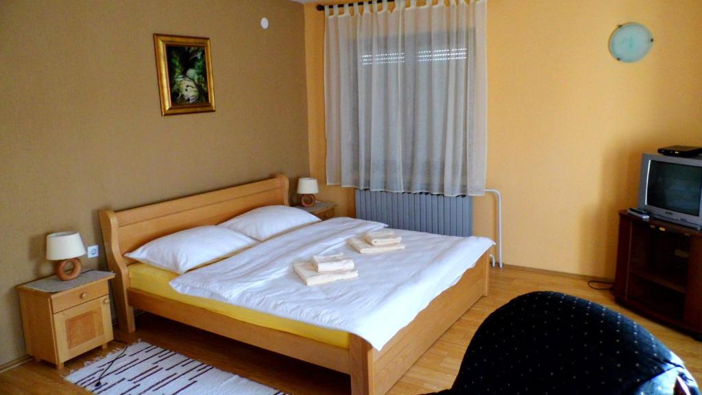 a bedroom with a bed with white sheets and a tv at Apartmani Maraton in Vukovar