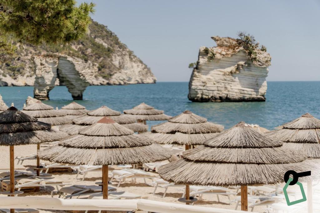 a group of straw umbrellas and chairs on a beach at HOTIDAY Room Collection - Mattinata Faraglioni in Mattinata