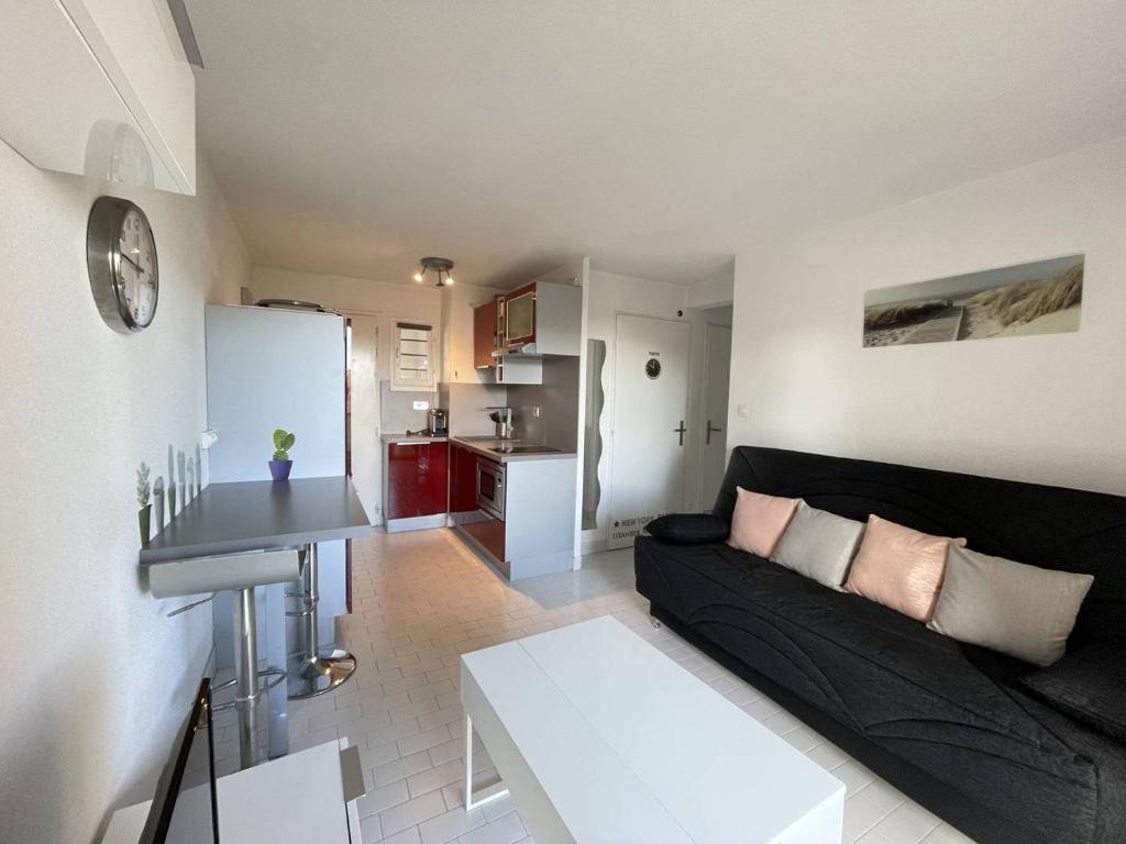 un salon avec un canapé noir et une cuisine dans l'établissement APPARTEMENT AVEC CHAMBRE ET CABINE SEPAREE À DEUX PAS DES PLAGES, au Cap d'Agde