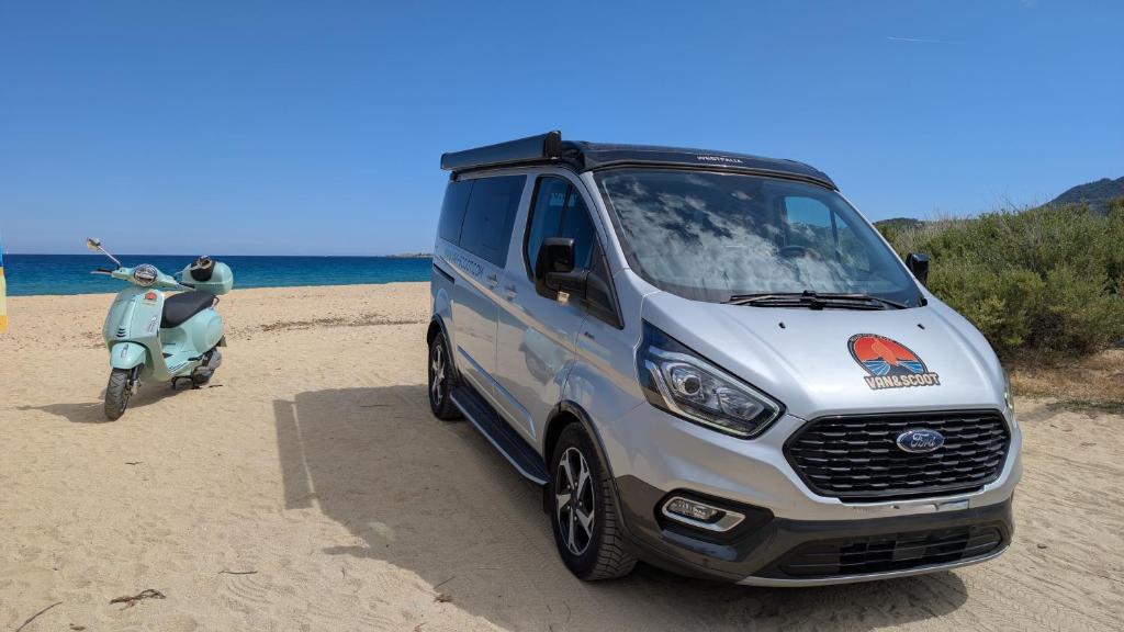 une camionnette argentée garée sur la plage à côté d'un scooter dans l'établissement Van&Scoot, à Belgodère