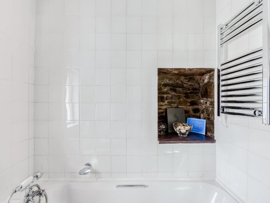 a white tiled bathroom with a tub and a laptop at Secluded Holiday Home in Ceredigion with Garden in Pennant