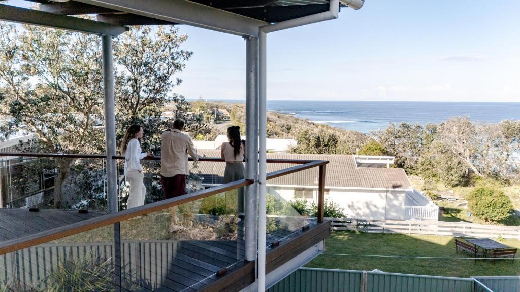 a group of people standing on a balcony looking out at the ocean at Rennies Beach House - Luxe Coastal Stay in Ulladulla
