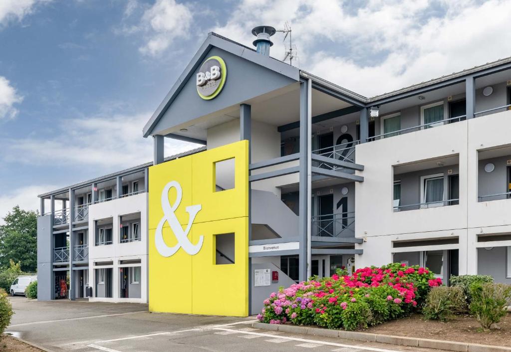 an office building with a yellow sign and flowers at B&B HOTEL Dieppe in Saint-Aubin-sur-Scie