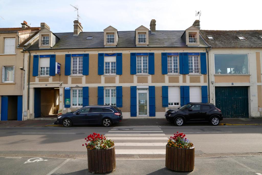 un edificio azul y blanco con coches estacionados frente a él en Maison Studios & Appartements Les 4 Vents, en Luc-sur-Mer