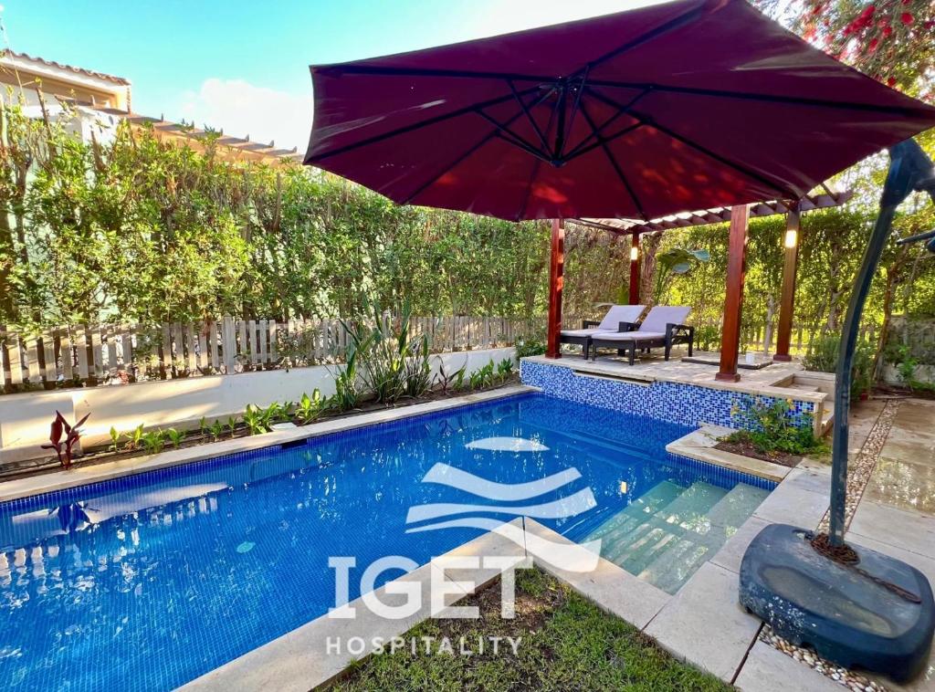 a blue swimming pool with an umbrella and a bench at Standalone with private pool in Marassi Victoria in El Alamein
