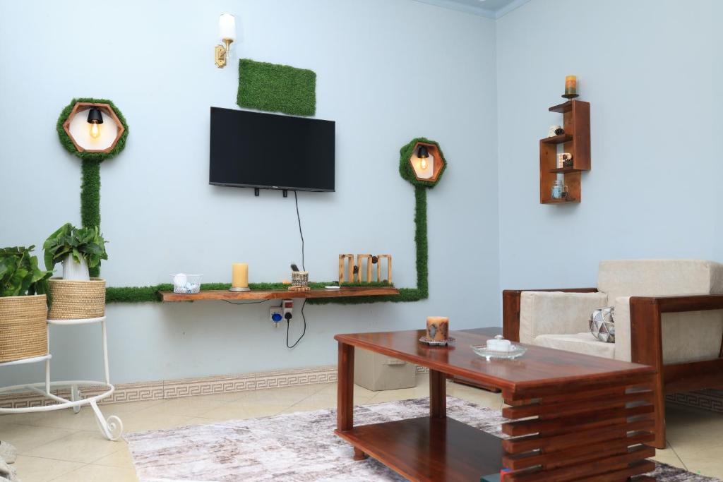 a living room with a table and a tv on a wall at Bethel Homz -Njeru in Buikwe